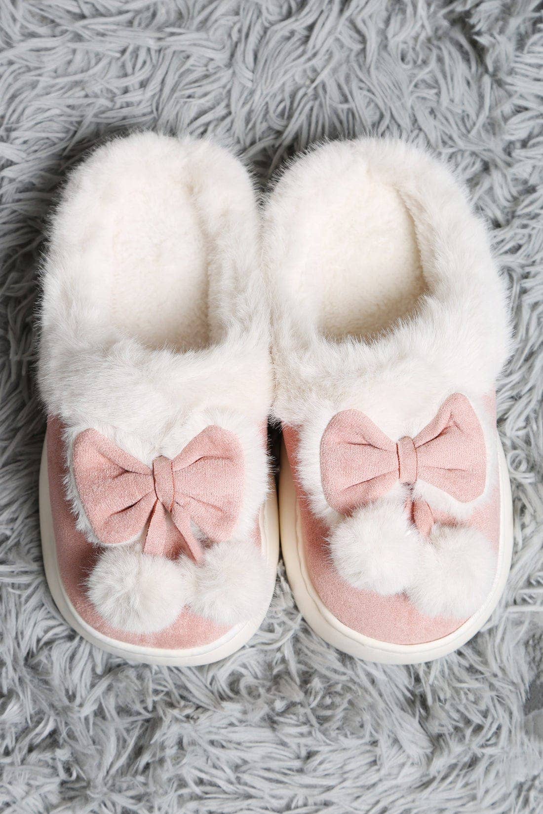 White slippers with pink bows and pom-poms on a gray textured surface