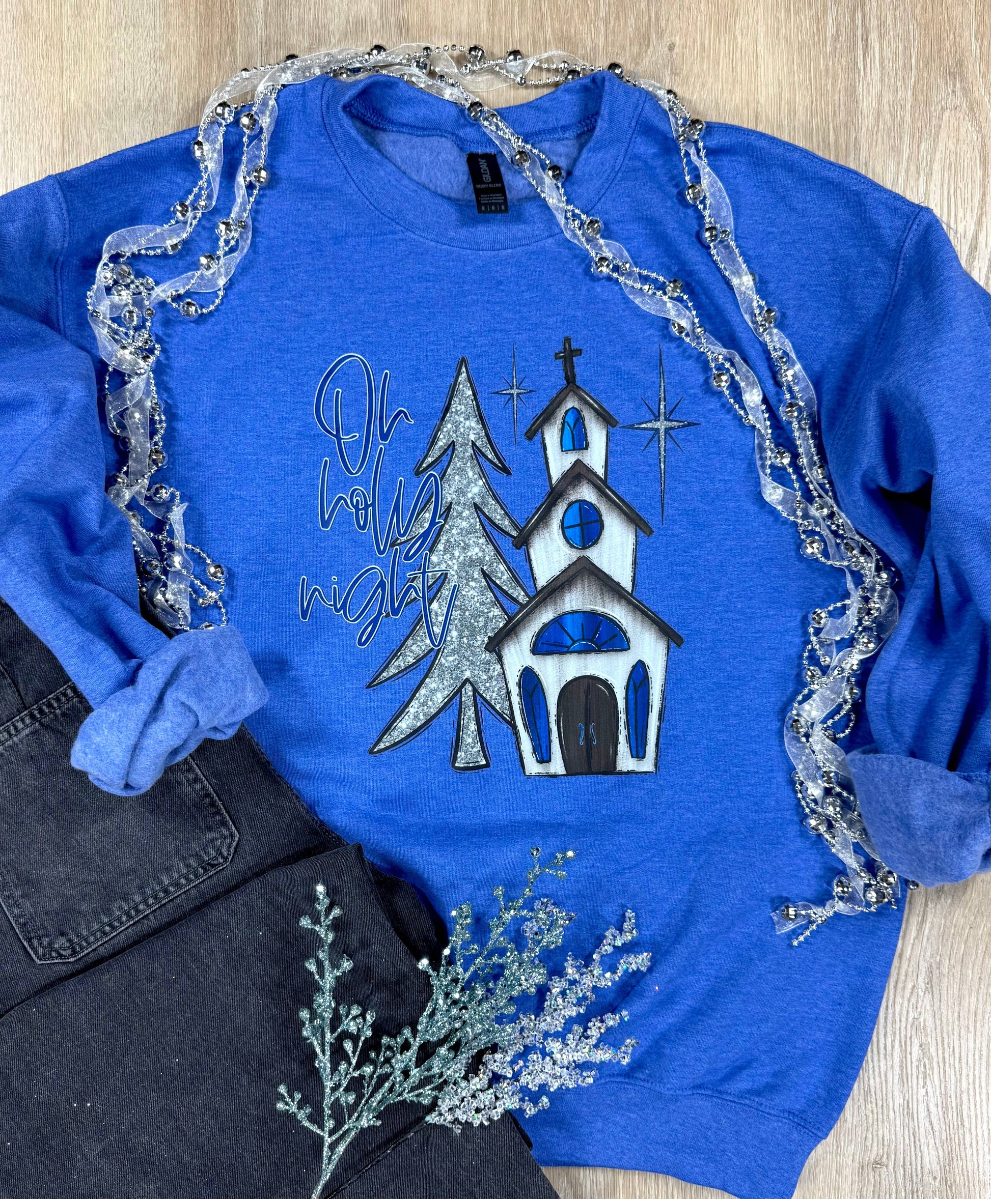Blue sweatshirt with Christmas design featuring a church and trees on a wooden surface.