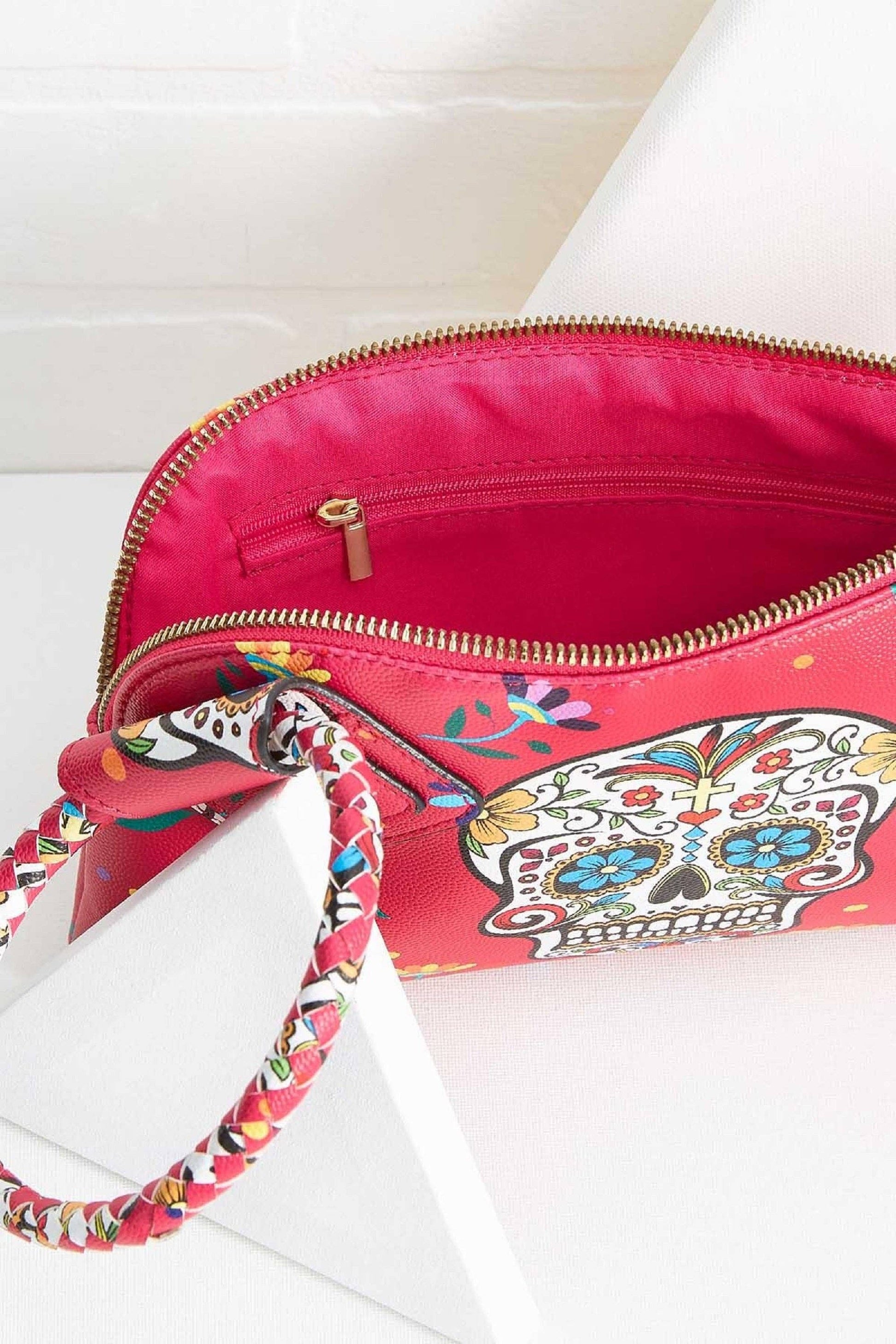 Pink handbag with floral strap and colorful skull design on a white background