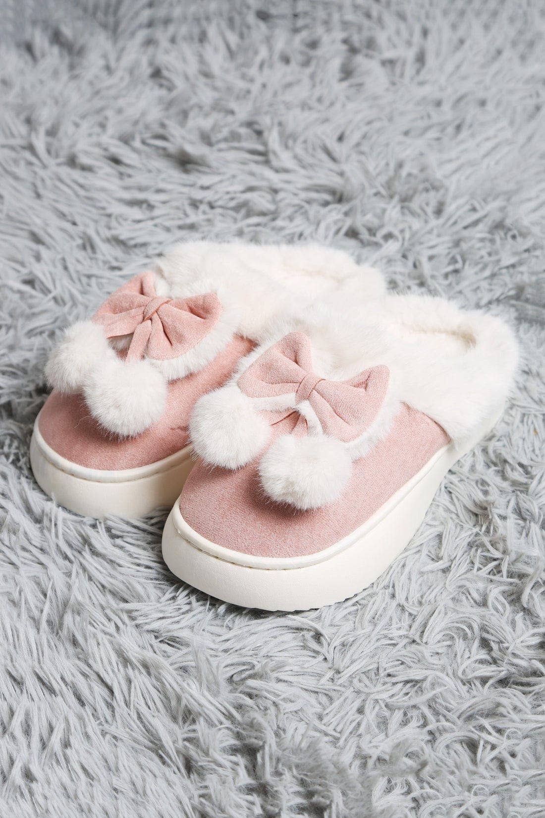 Pink slippers with white fur pom-poms on a gray fluffy surface