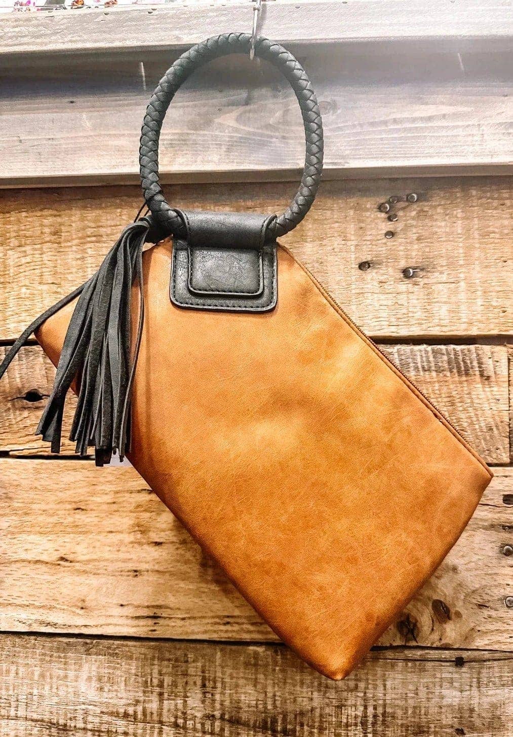 Brown leather handbag with black handle and tassel on a wooden surface