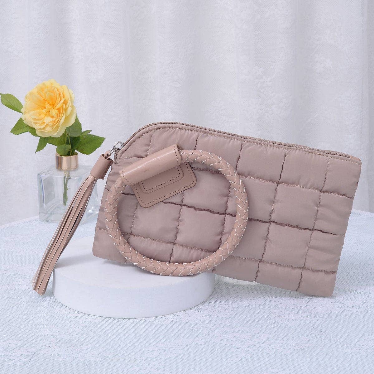 Taupe quilted handbag with circular handle on a white surface with a light gray background